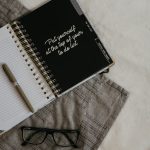 Stylish flatlay featuring a planner with quote, pen, and eyeglasses on a neutral background.